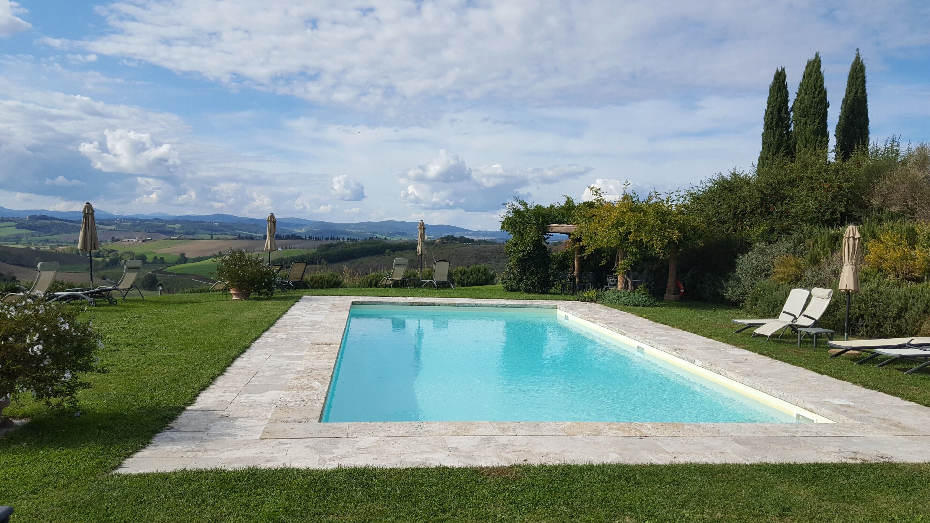 A rectangular swimming pool with a stone border, surrounded by a well-maintained lawn and several lounge chairs.