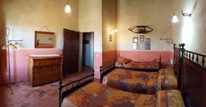 Une chambre avec deux lits, une commode en bois, un miroir et des lampes fixées au mur.