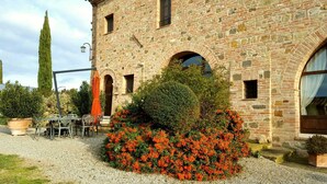 Un edificio de piedra con ventanas arqueadas y un sendero de grava que conduce a una zona de estar con una mesa y sillas.