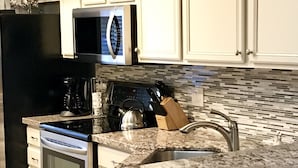 A kitchen with white cabinets, a black refrigerator, a microwave, a coffee maker, and a sink with a modern faucet.