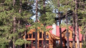 A log cabin with a stone chimney, wooden deck, and a view of a lake.