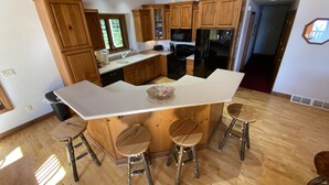 A modern kitchen with wooden cabinets, a central island with stools, and a view of the outdoors.