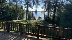 A wooden deck overlooking a lake with tall trees and a dock.