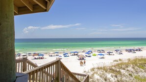 A beach with a wooden deck overlooking the ocean, featuring beach umbrellas and tents.
