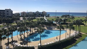 A resort with a swimming pool surrounded by palm trees and lounge chairs, overlooking a beach and ocean.
