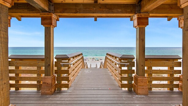 A wooden beach deck with railings leading to the shore.