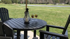 Une table ronde surmontée d’un parasol à rayures, deux verres remplis de boisson et une bougie, le tout placé sur une terrasse donnant sur un terrain de golf.