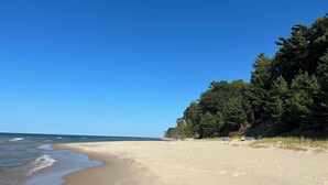 Uma praia com céu claro, águas calmas e uma área arborizada.