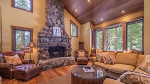 A cozy living room with a stone fireplace, leather furniture, and large windows offering a view of the outdoors. - Perfect Family Getaway With A/C - Location! Location! (Homewood)