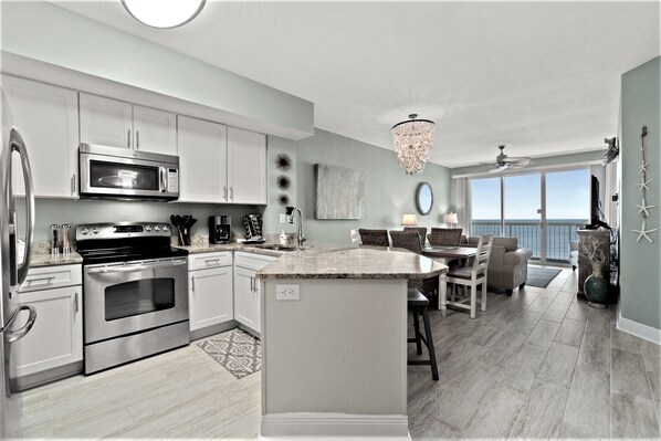 A modern kitchen with stainless steel appliances, a dining area with a view, and a chandelier. - GULF FRONT *Renovated* 3 BR (2 King Suites) + Beach Chair Svc.  Owner Managed! (Panama City Beach)