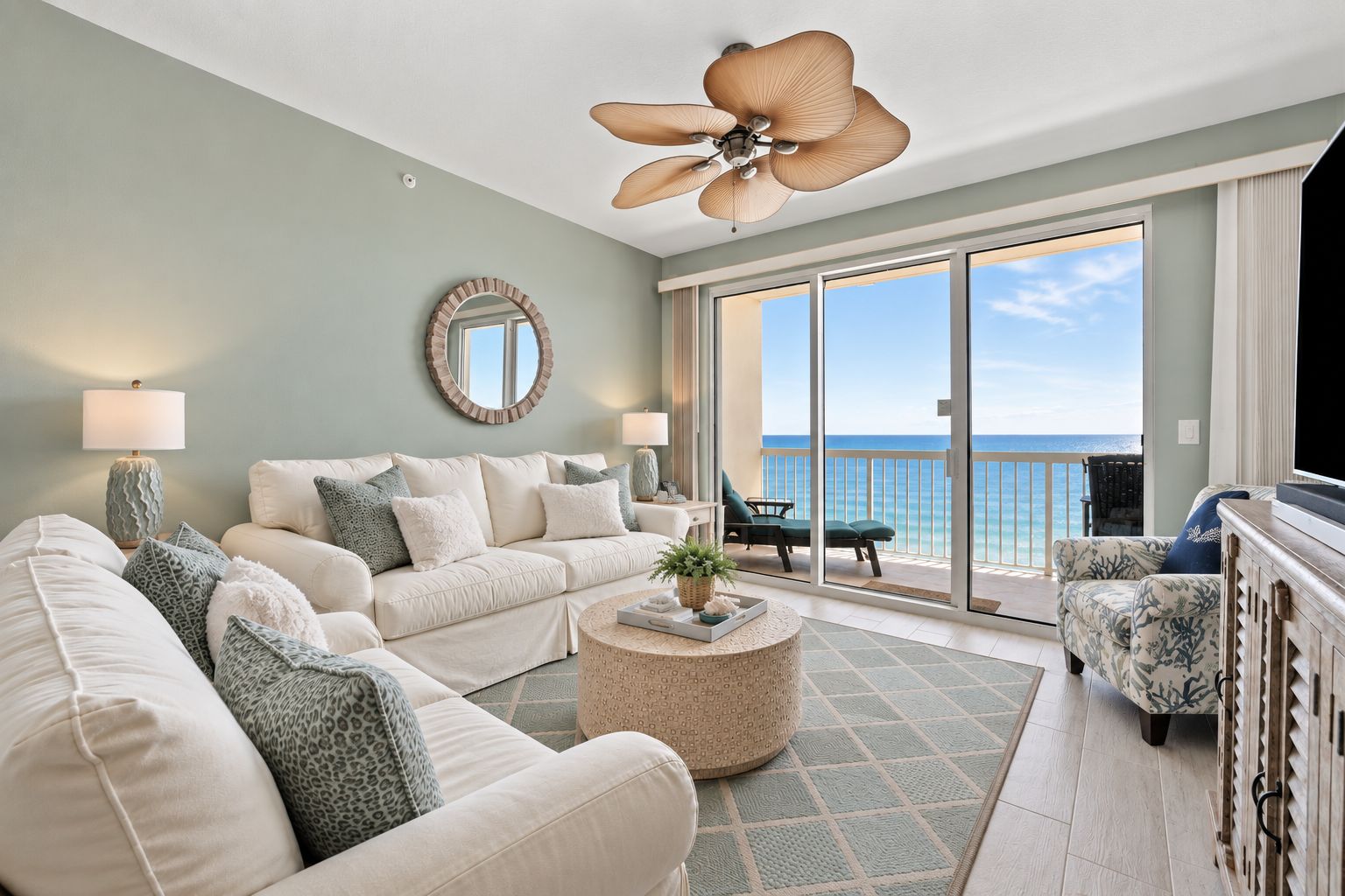A spacious living room with a large sofa, a coffee table, and a balcony with a view of the ocean.