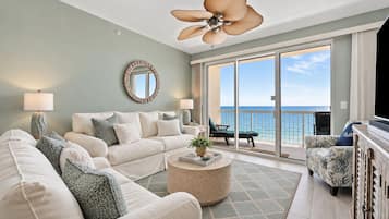 A spacious living room with a large sofa, a coffee table, and a balcony with a view of the ocean.