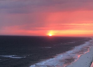 Un coucher de soleil sur l’océan, avec une plage au premier plan.