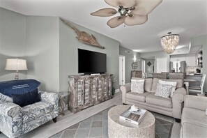 A living room with a sofa, a coffee table, a television, and a ceiling fan. - GULF FRONT *Renovated* 3 BR (2 King Suites) + Beach Chair Svc.  Owner Managed! (Panama City Beach)