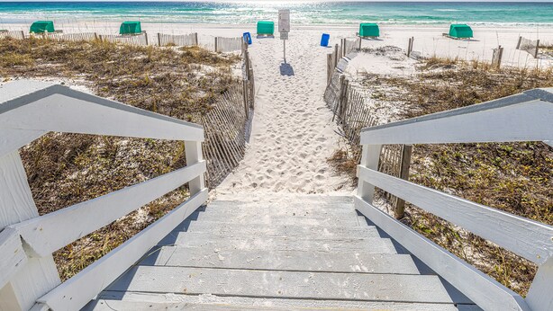 A wooden staircase leading to a sandy beach with a wooden fence and green chairs. - Oceanfront Elegance, Great Views, on the beach, steps to the sand 2BR/2BA (Destin)
