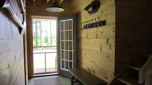 A wooden cabin interior with a door leading outside, a bench, a wall-mounted coat rack, and a ceiling light fixture. - Grey Goose Cottage In The Heart Of The FingerLakes (Keuka Lake Penn Yan)