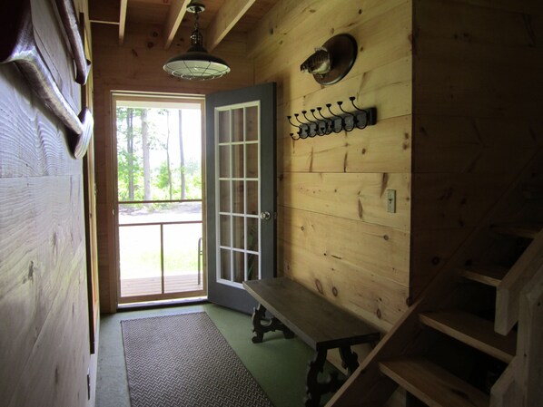 A wooden cabin interior with a door leading outside, a bench, a wall-mounted coat rack, and a ceiling light fixture. - Grey Goose Cottage In The Heart Of The FingerLakes (Keuka Lake Penn Yan)