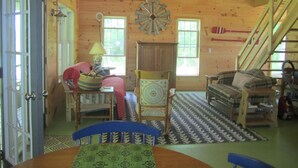 A cozy cabin interior with wooden walls, a dining table, two chairs, a sofa, a patterned rug, and a ceiling fan. - Grey Goose Cottage In The Heart Of The FingerLakes (Keuka Lake Penn Yan)
