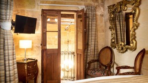 A hotel room with a bed, a television, a wooden door, a mirror, and a chair. - The 3Cities Auberge (Cospicua)