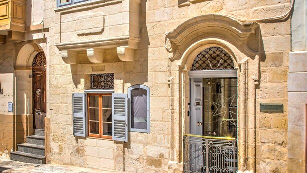 A historic building with a stone facade, multiple windows with shutters, and a central arched doorway. - The 3Cities Auberge (Cospicua)