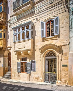 A historic building with a stone facade, multiple windows with shutters, and a central arched doorway. - The 3Cities Auberge (Cospicua)