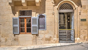 A stone building with multiple windows, some with shutters, and a decorative archway. - The 3Cities Auberge (Cospicua)
