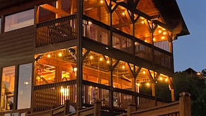 A wooden cabin with a balcony, large windows, and string lights.