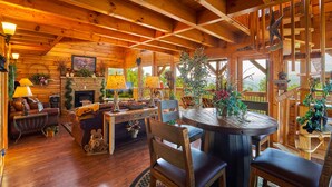 A cozy cabin interior with wooden walls, a fireplace, a dining area, and a view of the outdoors.