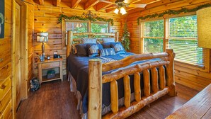 A log cabin bedroom with a wooden bed, a nightstand, a lamp, and a window with blinds.