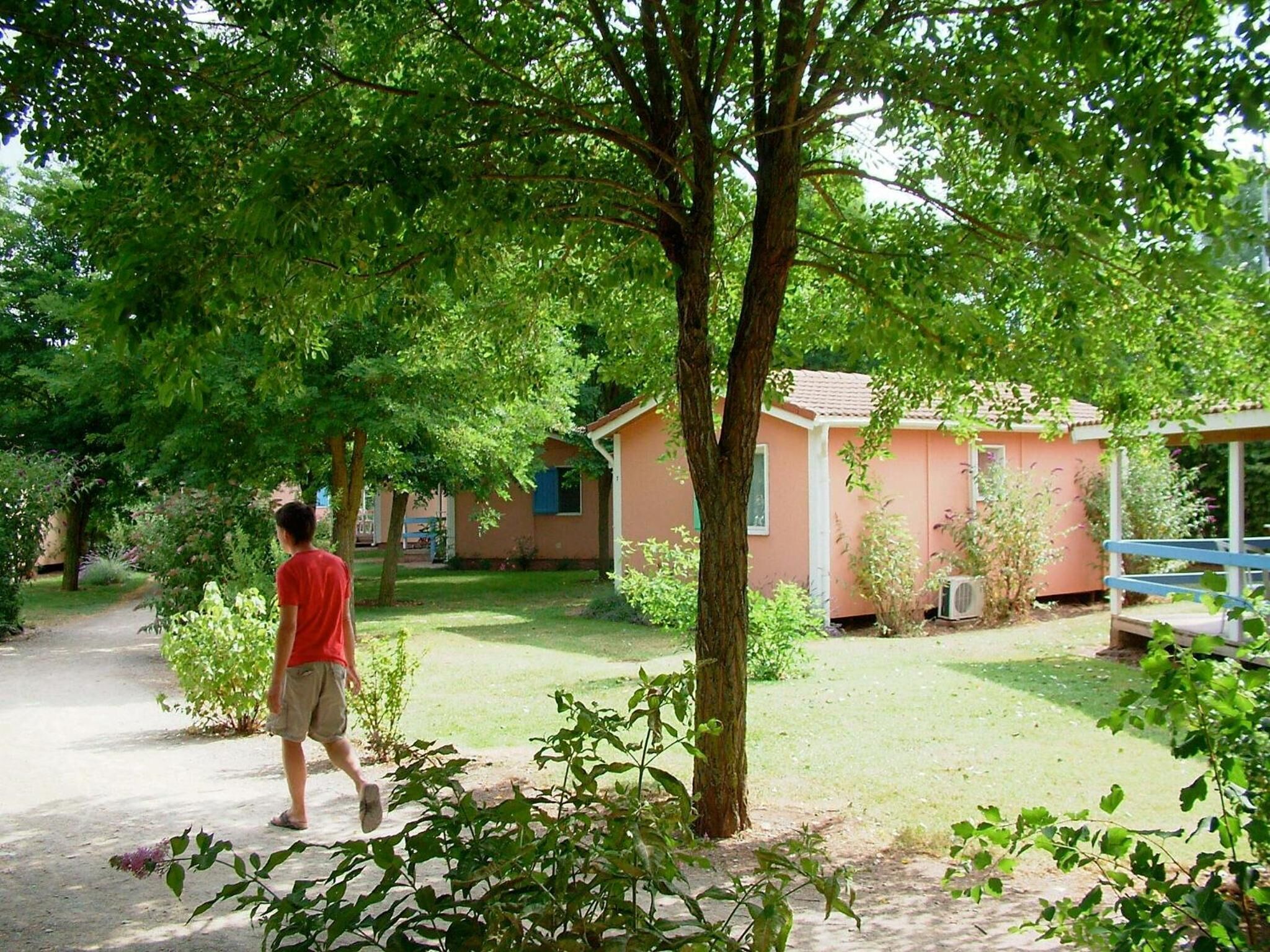 Une personne se promène sur un sentier dans un jardin, avec un petit bâtiment et un arbre au premier plan.