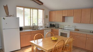 A kitchen with wooden cabinets, a white refrigerator, a microwave, a stove, and a dining table with chairs.