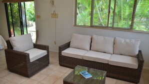 A wicker sofa with white cushions and a glass coffee table with a book.