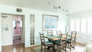 A dining area with a wooden table and chairs, a framed picture on the wall, and a window with blinds.