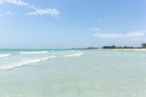 A beach with clear turquoise water, a sandy shore, and a distant city skyline.
