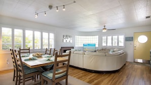 A spacious living room with a large white sectional sofa, a dining table with chairs, and a television.