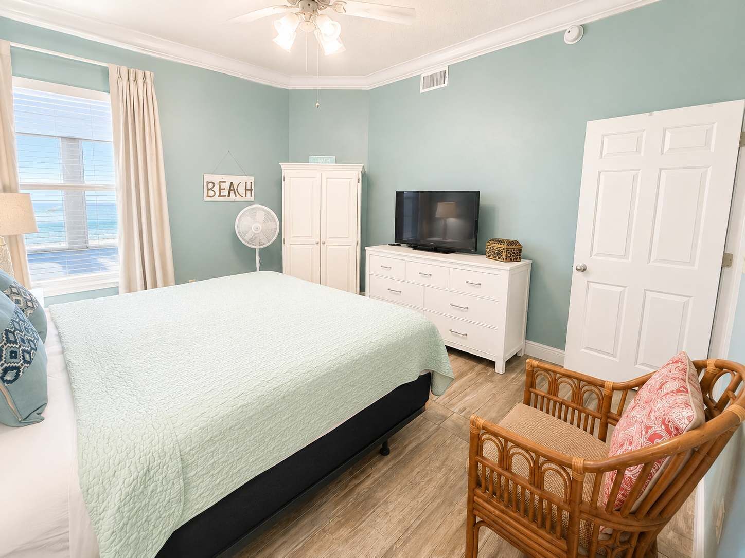 A bedroom with a bed, a television on a dresser, a fan, and a chair.