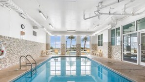 An indoor swimming pool with clear views of palm trees and a tiled wall.