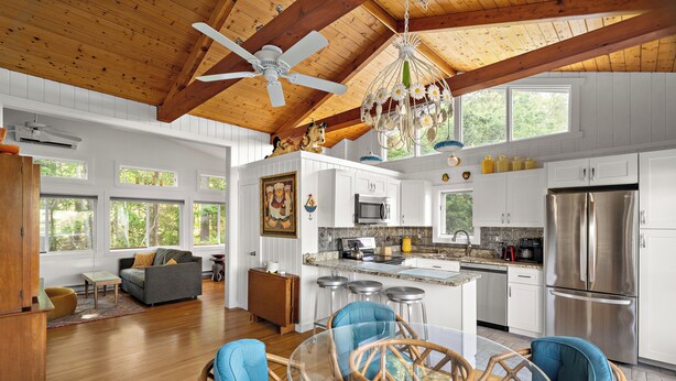 A spacious kitchen with white cabinets, a stainless steel refrigerator, and a dining area with wicker chairs and a glass table. - Ogunquit Cottage - walk to beach (Ogunquit)