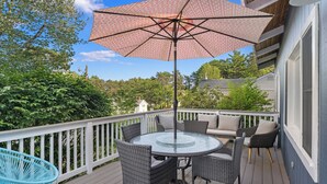 A deck with a round table and chairs, a large umbrella, and a white railing. - Ogunquit Cottage - walk to beach (Ogunquit)