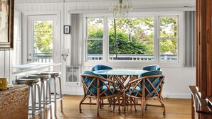 A spacious room with a wooden ceiling, a dining table with blue chairs, and large windows offering a view of greenery outside. - Ogunquit Cottage - walk to beach (Ogunquit)
