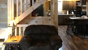Un interior espacioso de madera con una escalera que conduce a un nivel superior, una zona de estar acogedora y una cocina con armarios de madera.