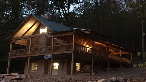 Une cabane en rondins dotée d’une grande véranda et de nombreuses fenêtres, entourée d’arbres.