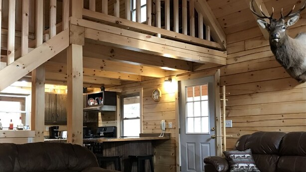 Interior rústico de una cabaña con una escalera de madera, una zona de cocina y una sala de estar amueblada con sofás de cuero.