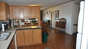 A kitchen with wooden cabinets, a dining area with chairs, and a refrigerator. -  For Larger Groups Up To 24, Right on Reelfoot Lake--Private Dock And Pier. (Hornbeak)