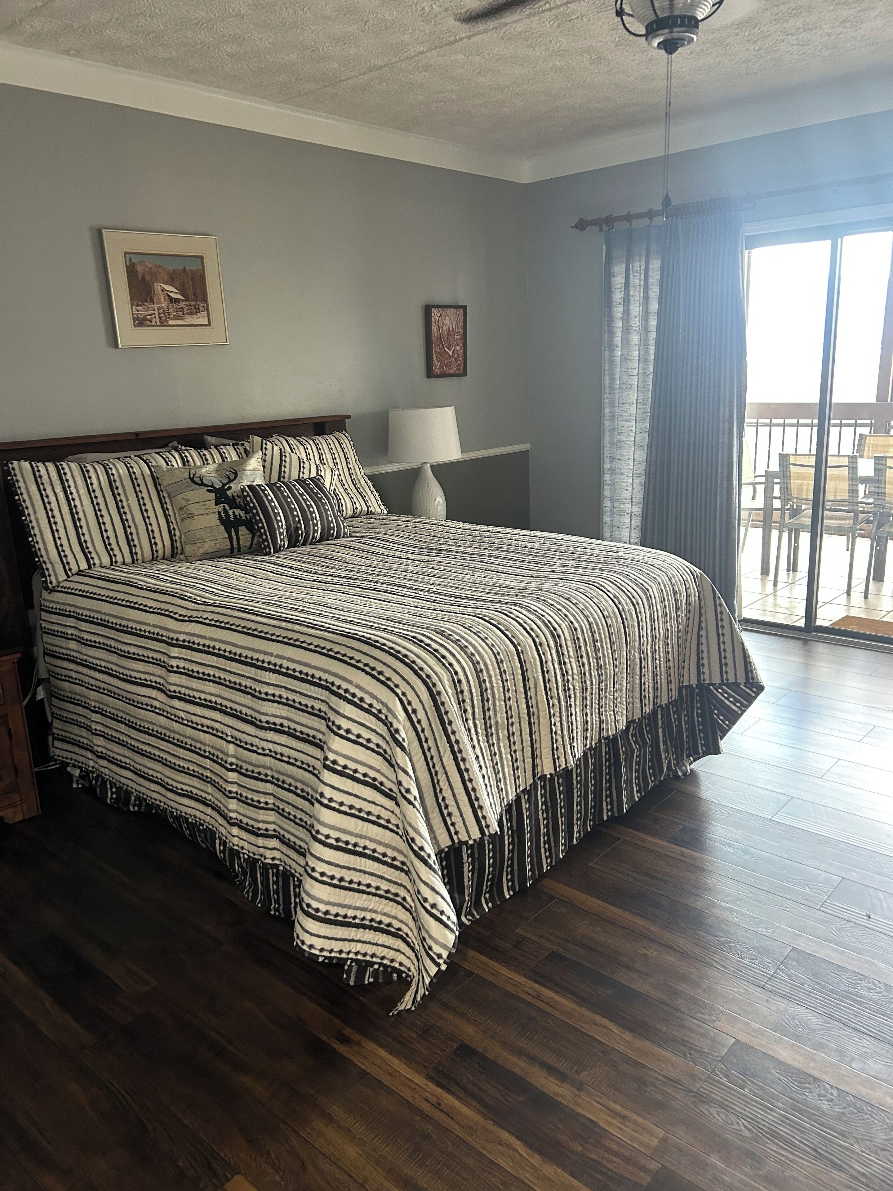 A bedroom with a large bed, a nightstand, a lamp, and a ceiling fan.
