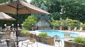 A poolside area with a stone wall, lounge chairs, and a table with an umbrella. - Right beside pool (Gatlinburg)