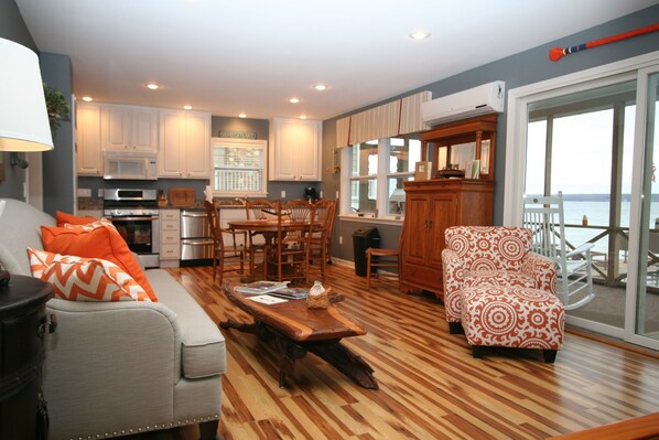 A modern kitchen with white cabinets, a dining area with wooden chairs, a grey sofa with orange pillows, and a wooden coffee table. - 'Getg Inn' Comfortable Cozy Lakefront Property-Beautiful View (Penn Yan)