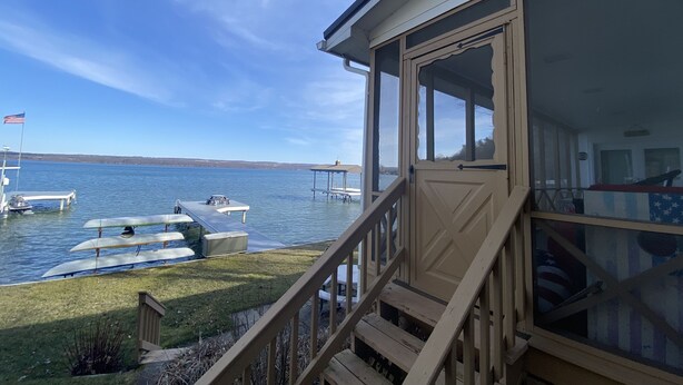 Eine Blockhütte am Seeufer mit einer Terrasse, einer Veranda und Blick auf See und Boote.