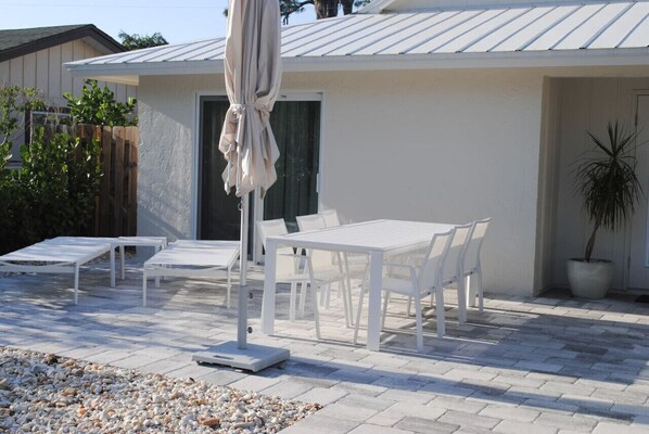Une terrasse dotée de mobilier blanc, comprenant des tables et des chaises, et agrémentée d’un parasol.