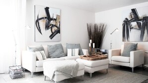 Un salon moderne avec un canapé blanc, des œuvres d’art abstraites accrochées aux murs et un vase décoratif contenant des bougies.
